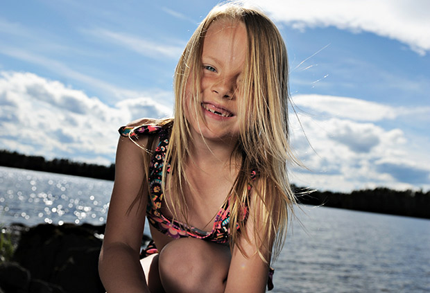Bild på leende flicka framför solglittrig sjö