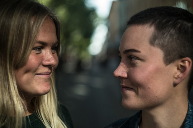 Närbilder på två yngre kvinnor som tittar på varandra. De befinner sig i en stadsmiljö.