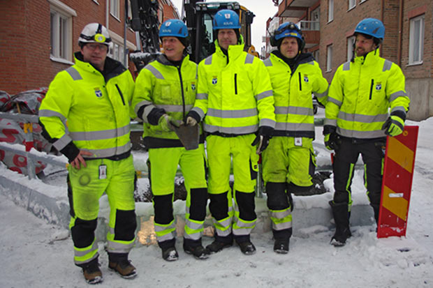 Fem rörläggare i gula varselkläder framför en grop och en grävmaskin på Prästgatan