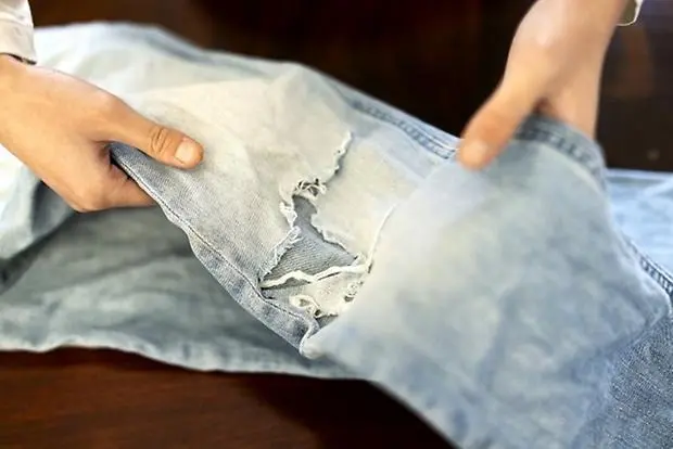 Händer som håller i ett par ljusblå jeans som är trasiga på knät.