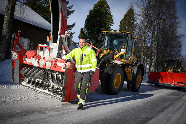 Foto: En man i varselkläder står i solskenet framför en snöslunga