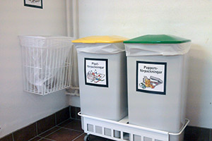 Två små tunnor för plast- och pappersförpackningar samt en korg på väggen för Sopor till förbränning