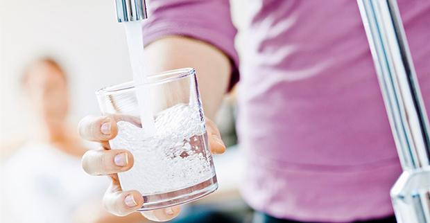 Person med rosa tröja fyller i vatten i ett glas från en vattenkran.