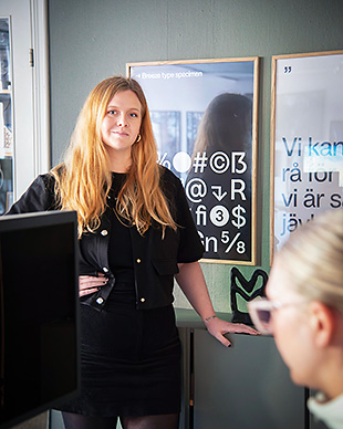 Presentation i mötesrum. Person står framför skärmar och talar till deltagare.
