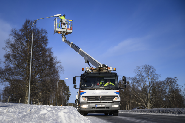 En man står i en skylift och arbetar med en gatlyktas armatur