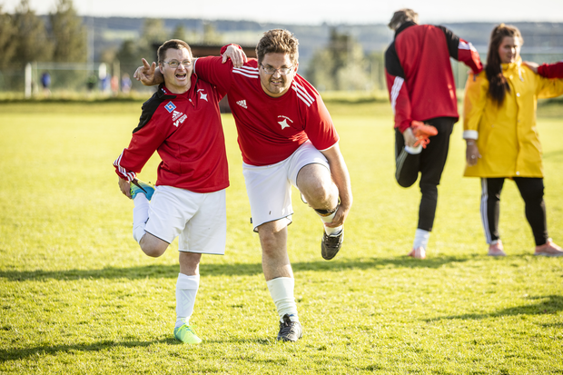 Personer i träningskläder stretchar på fotbollsplan