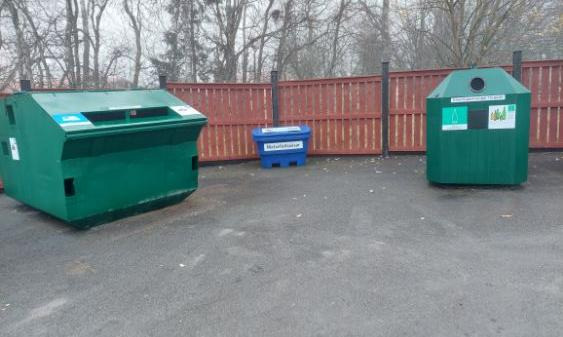 Två gröna containrar med en blå låda emellan och ett rött plank bakom.