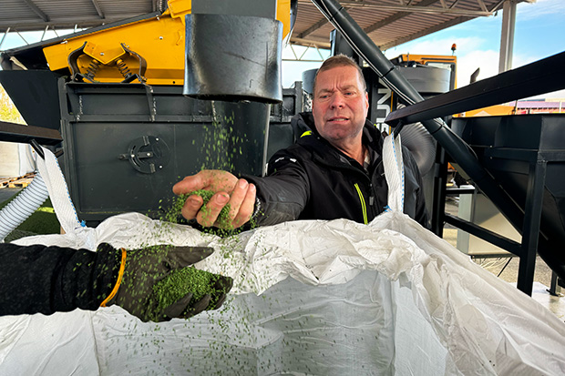 En person sträcker fram handen och fångar upp renat granulat som åker ur maskinen.