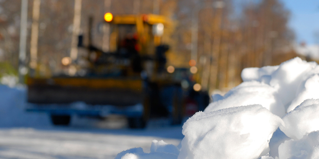 Foto: Snöröjningsfordon kommer längs gata med snöhög i förgrunden.