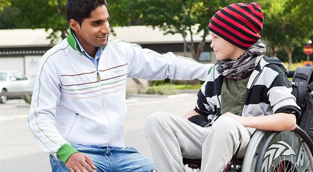 Mörkhyad kille hjälper ung pojke som sitter i rullstol