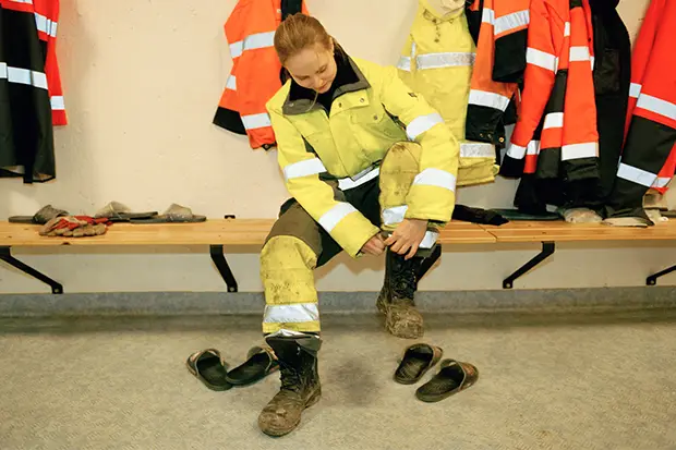 Ung kvinna i gula varselkläder sitter på en bänk och tar på sig kängor