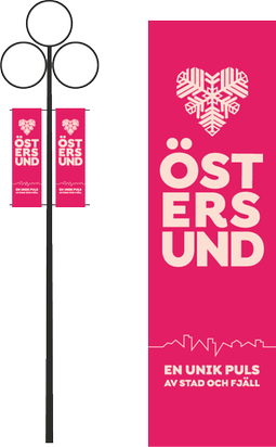 Mörkt rosa flaggor med Östersundslogotypen, pulsen och en slogan. De två flaggorna är monterad på varsin sida av en lyktstolpe.