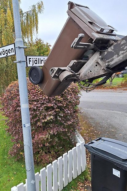 Brunt matavfallskärl lyfts upp av sopbilen. Kärlet tar i gatunamnsskylten eftersom det stått för nära stolpen. 