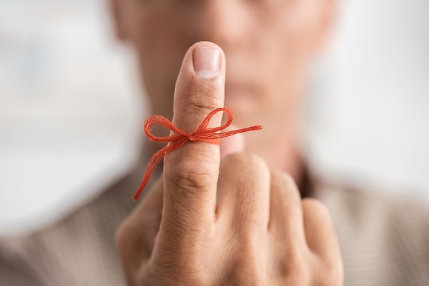 Oskarp person i fonden håller upp ett pekfinger med en röd minnesknut.