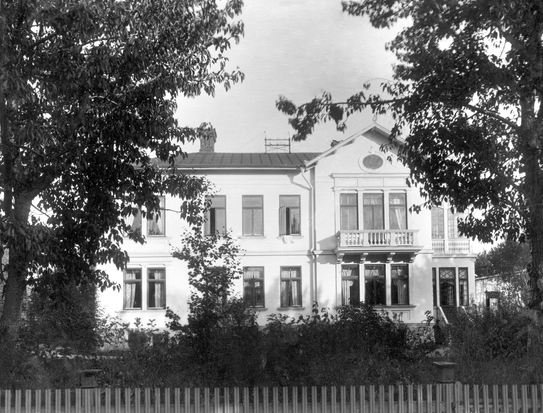 Gammal, svartvitt foto på en villa i två våningar med stora fönster.