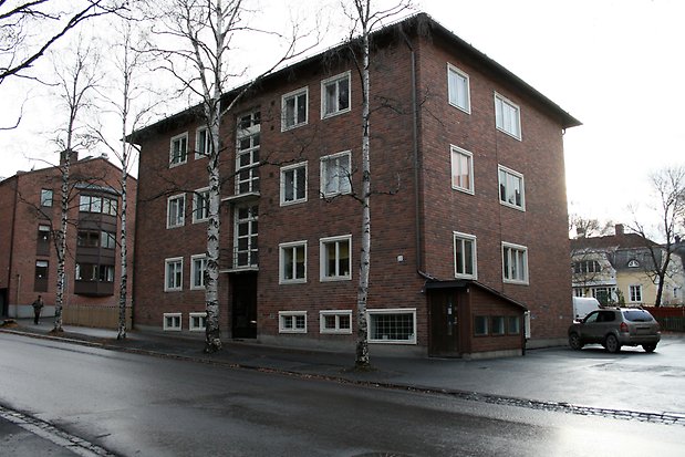 Fyrkantigt hus i brunt tegel. Fyra våningar. Vita fönster.