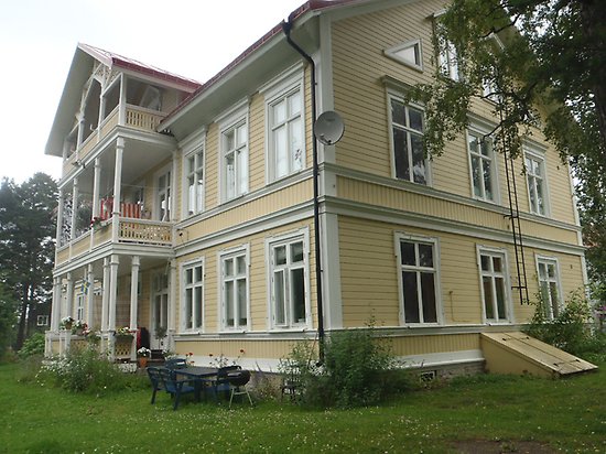 Rönnen 1. Villa i tre våningar, i ljusgul, liggande träpanel med två balkonger med snickarglädje och vita fönster med spröjs.