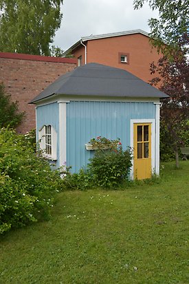 Solrosen 6. Litet hus i ljusblå panel med gul dörr och litet vitt fönster med spröjs.