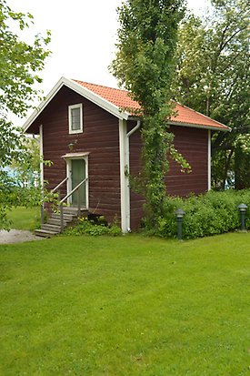 Solrosen 7. Timrat, brunt hus med grön dörr och ett litet, vitt fönster med spröjs.