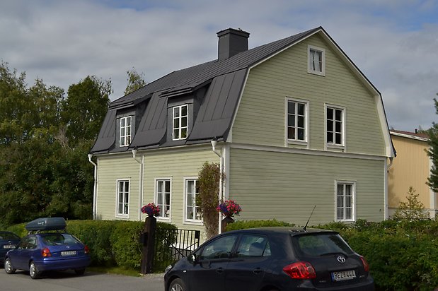 Vallmon 4. Villa med grön, liggande träpanel, vita fönster med spröjs och svart plåttak.