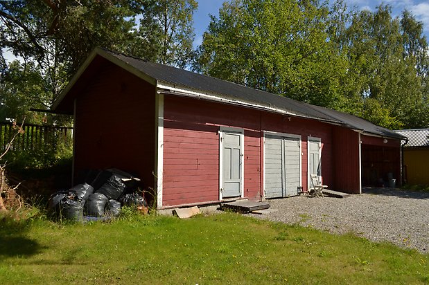 Sälgen 2, Byggnad i röd, liggande träpanel, med två dörrar och garageport i grönt.