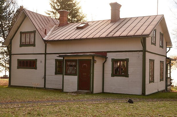 Hammarskiftet 5. Villa i ljusbeige, liggande panel, gröna detaljer och fönster, med röda spröjs. Rött plåttak. 