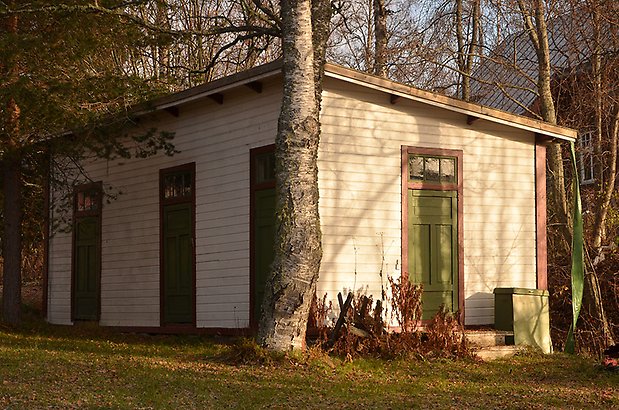 Hammarskiftet 5. Byggnad i ljusbeige, liggande panel med röda detaljer och gröna dörrar, sluttande tak. 