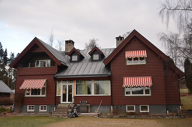 Hammarskiftet 9. Villa i brun, liggande panel med vita fönster och svart plåttak med takkupa. 