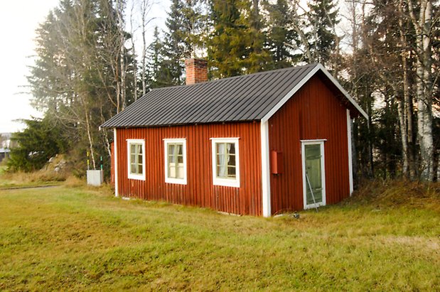 Rött hus med vita knutar och fönster med gröna spröjs.