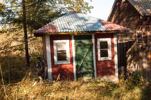 Liten röd byggnad med grön dörr och vita fönster.