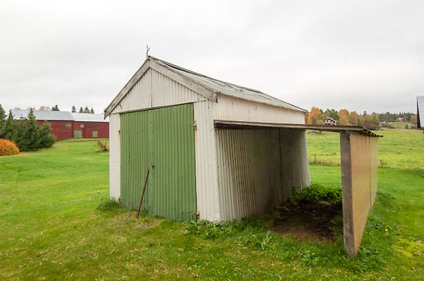 Byggnad i vit panel med grön dubbelport, med snedtak till höger.