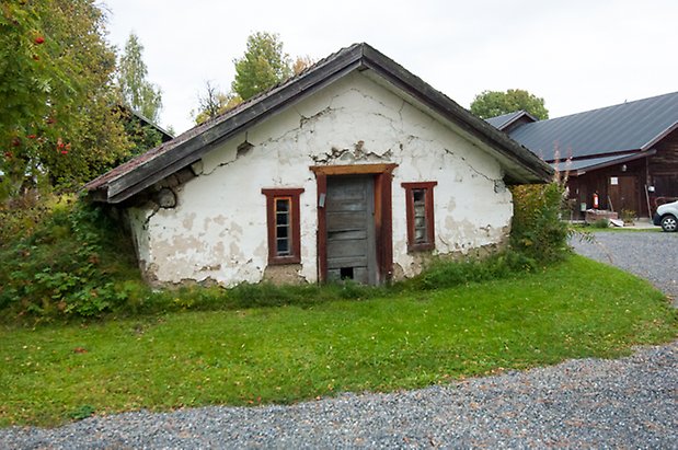 Vitputsad byggnad med sprucken byggnad med grå dörr och små fönster.