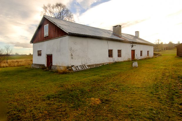 Byggnad i två våningar med vitputsad undervåning och övervåning i röd panel, med fönster med röda spröjs och röda portar.