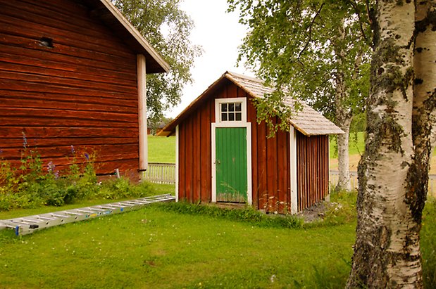 Liten byggnad i röd panel med grön dörr med ett litet fönster ovanför.