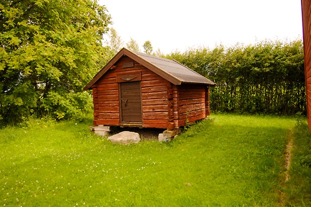 Liten röd timrad byggnad med port.