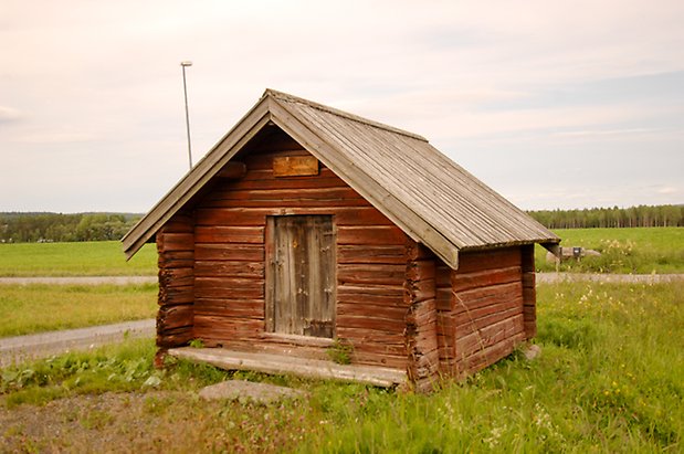 Liten röd timrad byggnad med lucka.