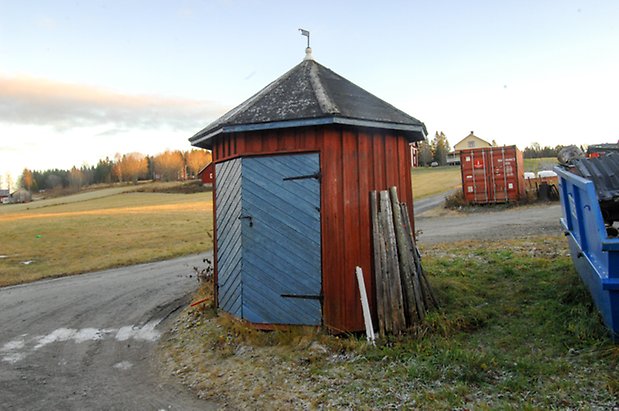 Litet åttakantigt hus i röd panel med blå dubbelport.