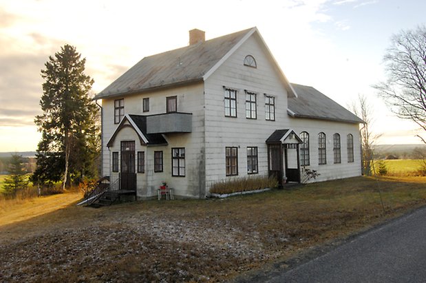 Hus i vitt, i tre våningar med brun dörr och fönster med bruna spröjs.