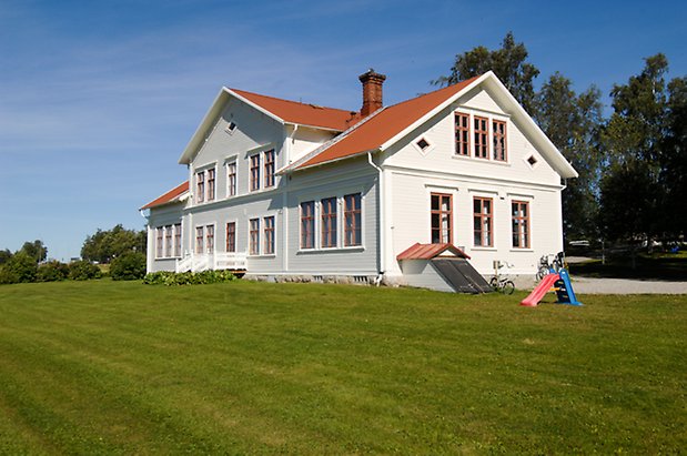Stort hus i vit liggande panel med fönster med orange spröjs.