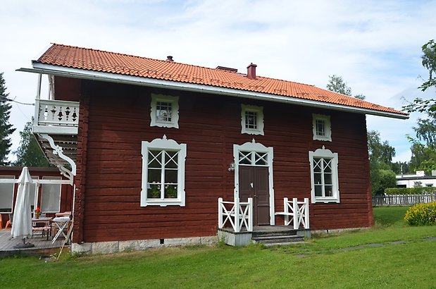 Byalaget 18 - Rött timrat hus med vita fönster med spröjs och snickarglädje.