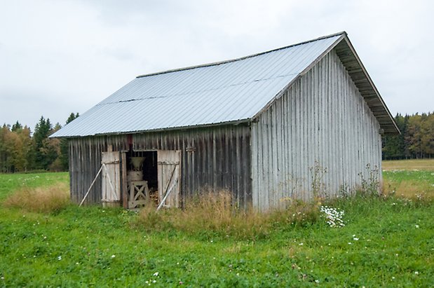 Boda 1:4. Byggnad i grånad träpanel med öppna portar.