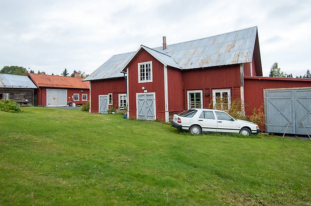 Boda 1:6. Byggnad i röd stående panel med tre blå dubbelportar och fönster med vita spröjs.