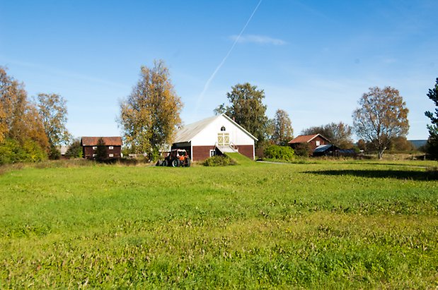 Fjäl 4:34. Ladugård i två våningar med röd liggande panel på undervåningen och vit stående panel och gröna dubbelportar.