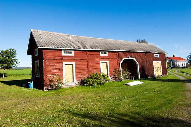 Handog 3:12. Timrad, rödmålad byggnad hopbyggd med byggnad i stående panel. Med gula dörrar och dubbelportar.