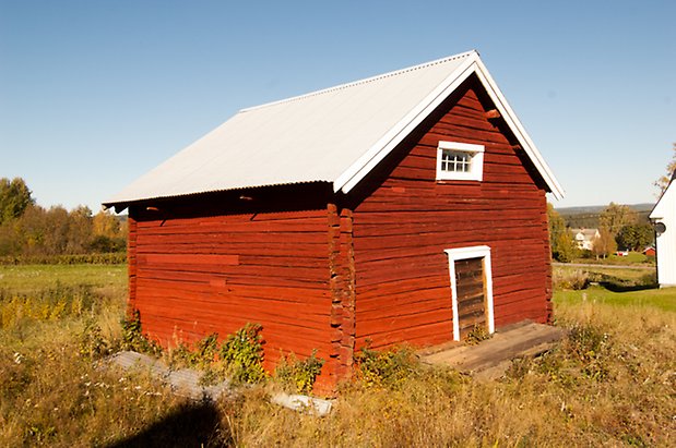 Hökbäck 1:13. Timrad, rödmålad byggnad med port och litet fönster.