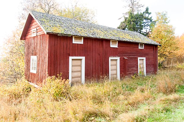 Hölje 4:7. Byggnad i röd panel och timmer med tre gula portar och fönster med vita spröjs.