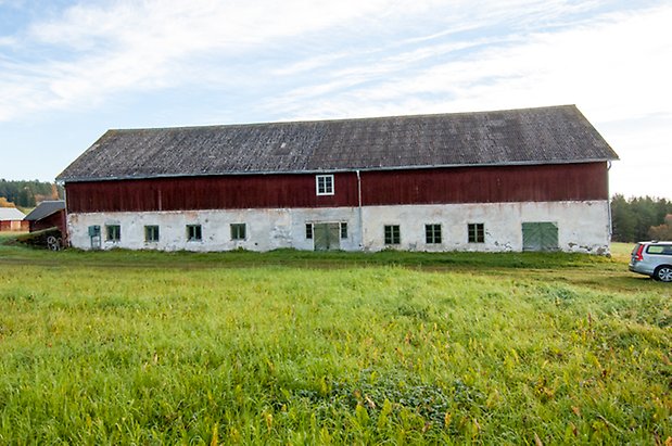 Hölje 4:7. Ladugård i två våningar, vit puts på undersidan och röd panel på övervåningen, två gröna portar och fönster med vita spröjs.