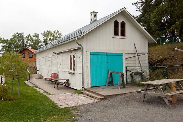 Klösta 6:5. Byggnad i vit panel med tre vita portar, fönster med röda spröjs och garageport i turkos.