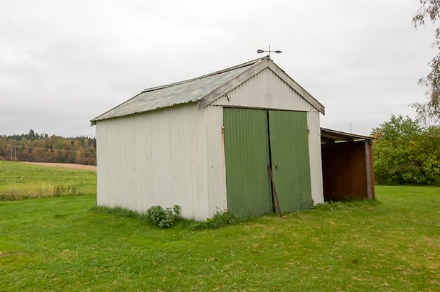 Korsta 2:15. Byggnad i vit panel med grön garagedörr. 