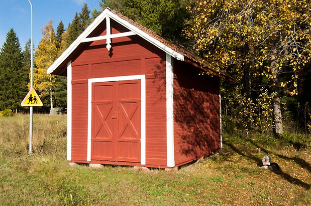 Lits-Bye 1:40. Liten byggnad i röd, liggande panel med en röd dubbelport.